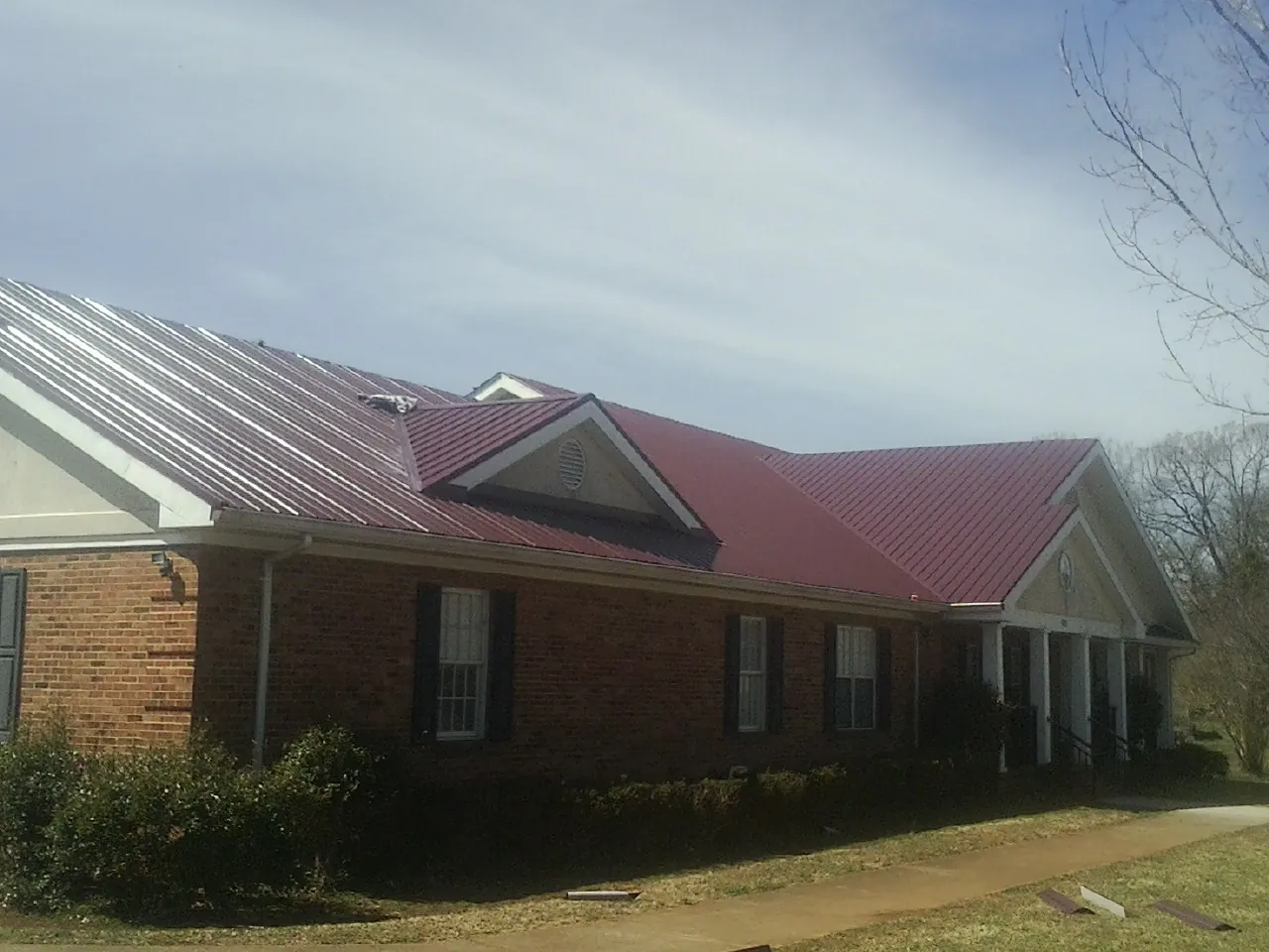 Red metal roof with gabled entries on a long brick building, from a Hail Damage Roof Repair job in Johnston