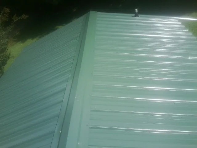 New green metal panels meeting at the ridge of a roof — Flat Roof Repair work by our crew in Johnston